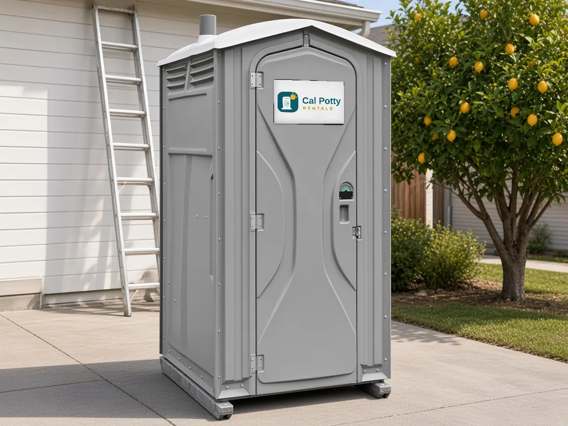 A grey porta potty beside a white house wall with a ladder and a lemon tree