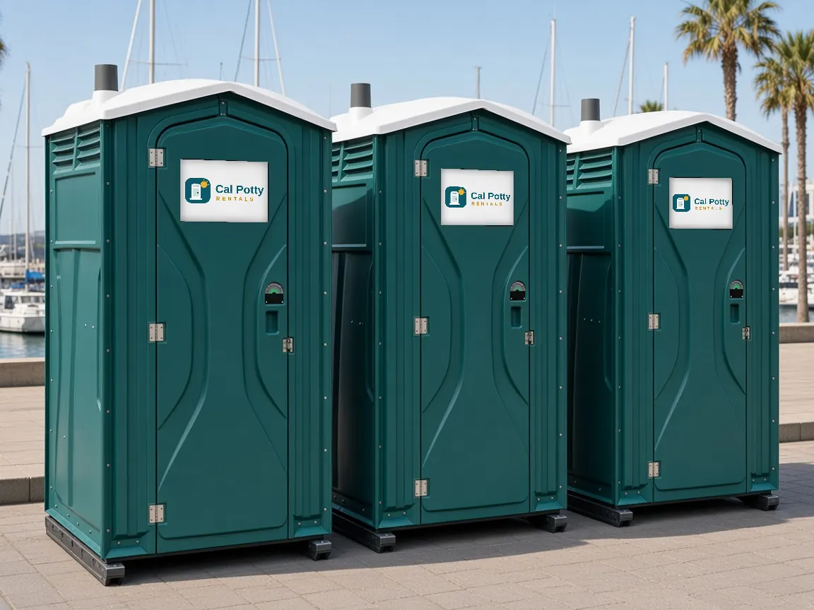 Three teal portable toilets on a waterfront promenade with sailboats behind